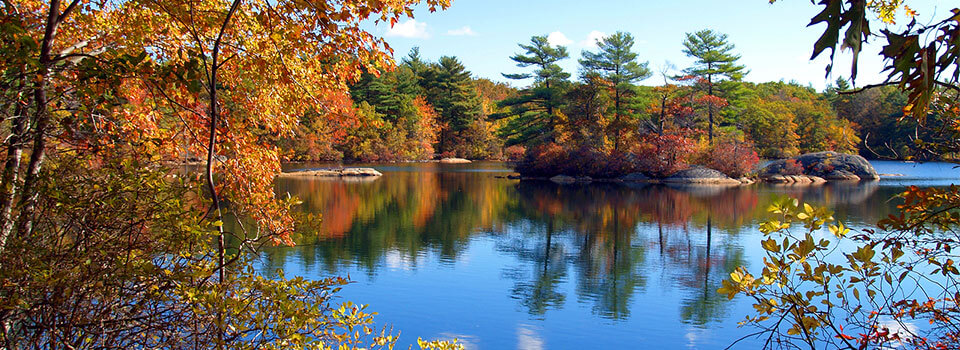 lake in early fall with green and orange leaves on trees and a small island in the middle